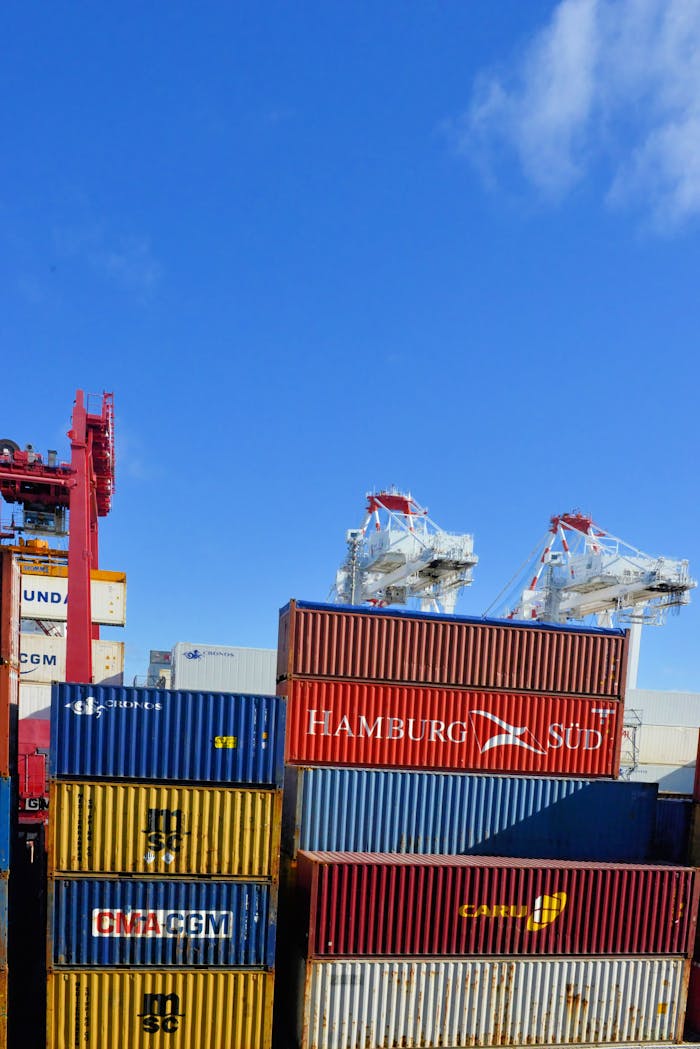brand-02 Colorful cargo containers stacked at a busy shipping port under a clear blue sky.